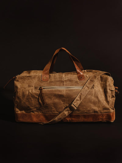Tan colored handcrafted canvas duffle bag with leather straps on black studio background.