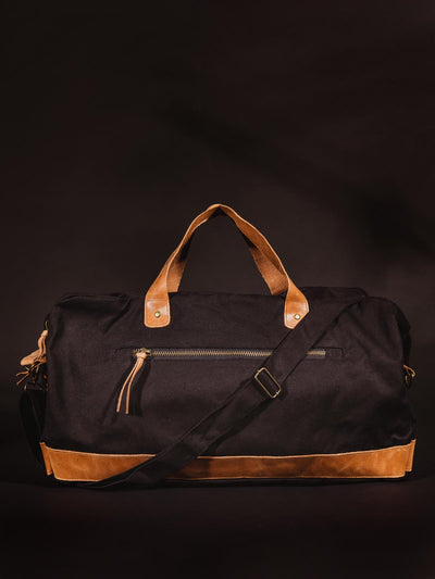 Black colored handcrafted canvas duffle bag with leather straps on black studio background.