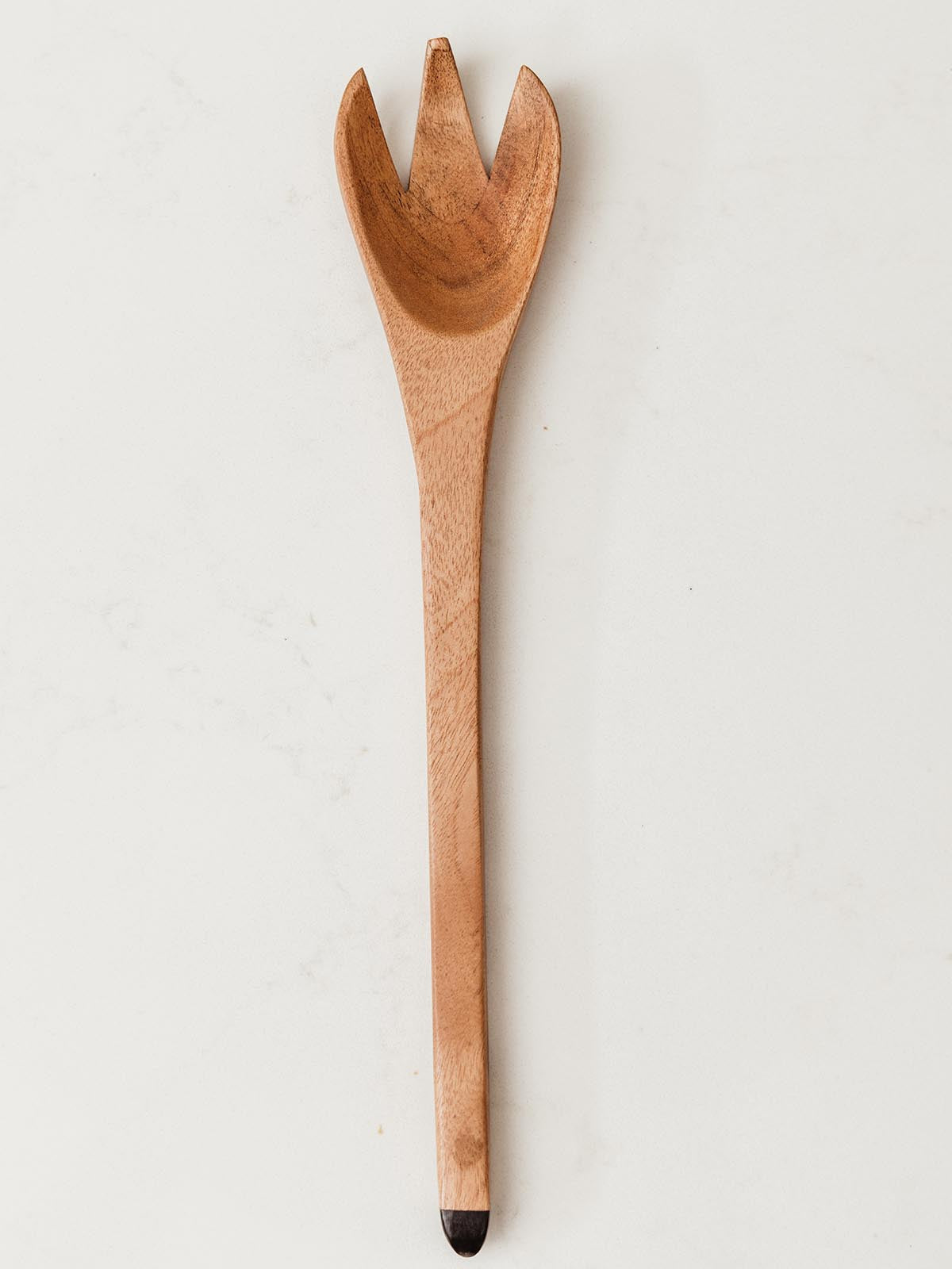 Serving spoon with forked end on white counter.