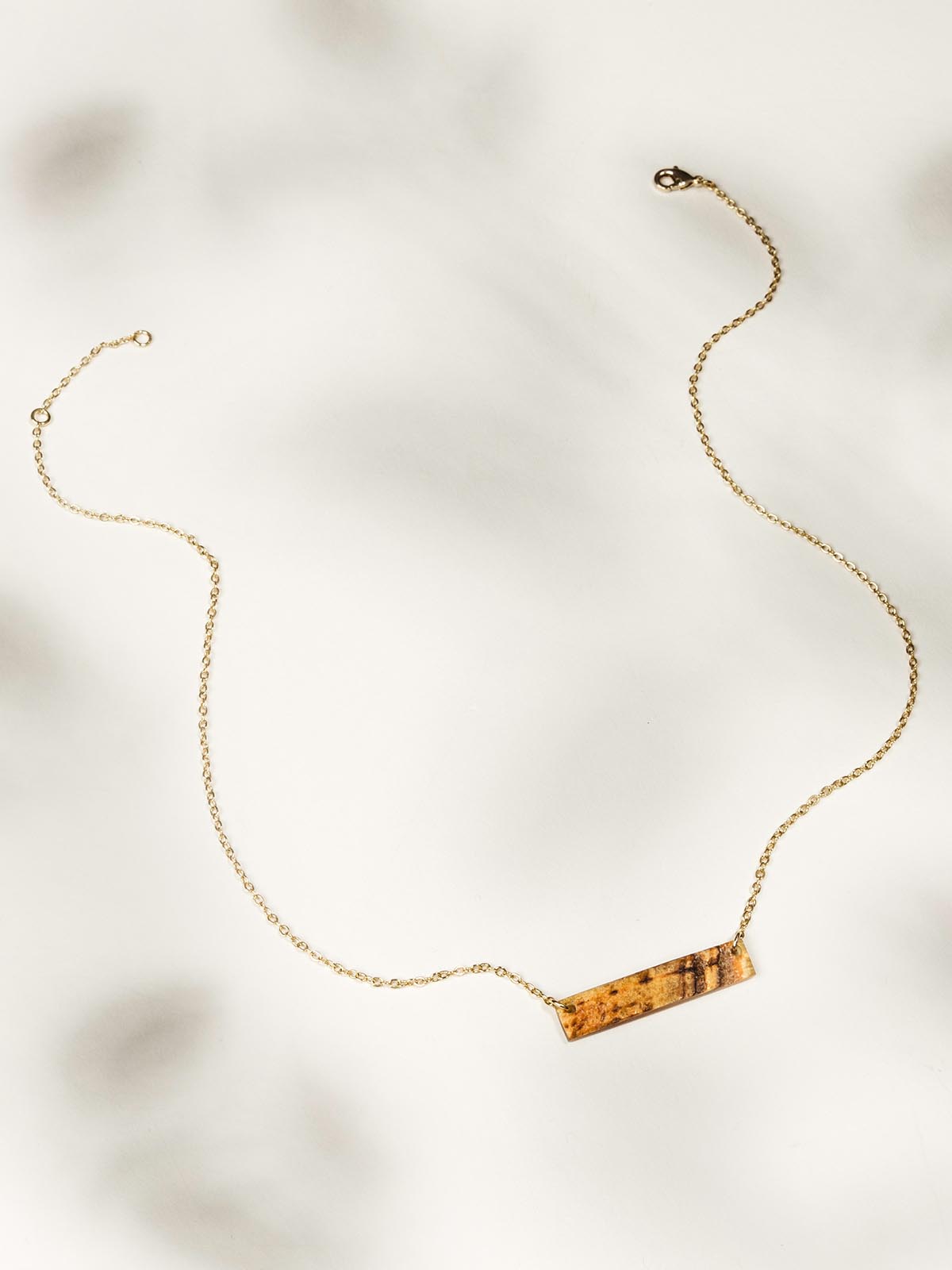 Medium length necklace with gold chain on a white background. Small rectangle textured pendant.