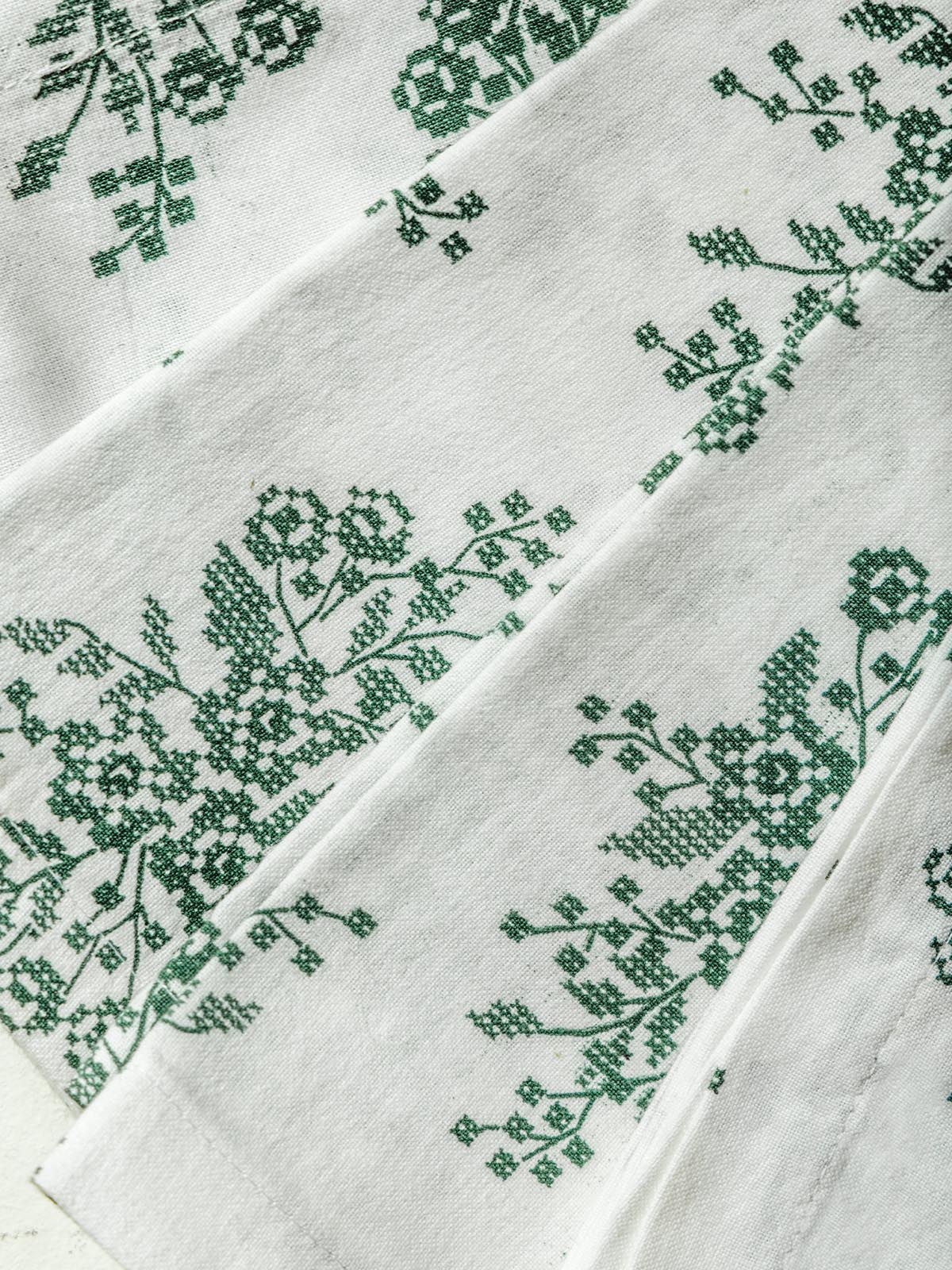 Close up details of white napkin with jade floral embroidery.