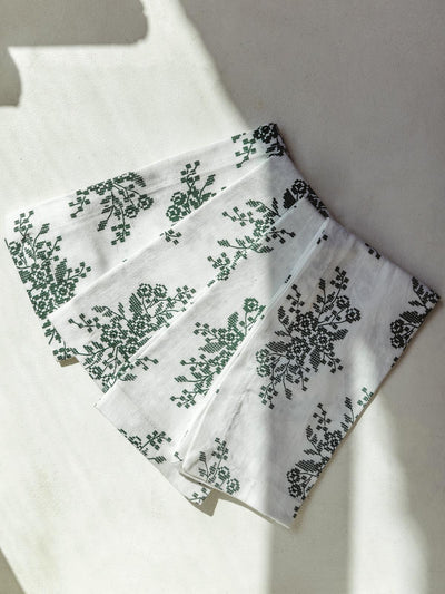 Four white napkins with floral jade embroidery on a cream surface.