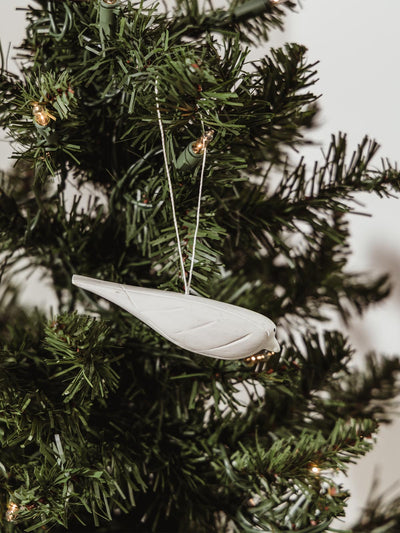 Small white wooden bird ornament tied to holiday tree with white string hanger. 
