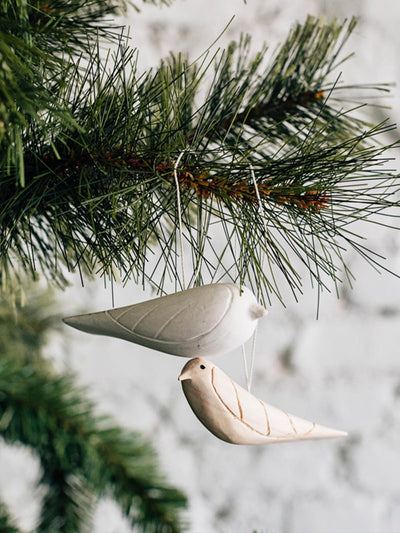 Two white wood bird ornaments hung on holiday tree.