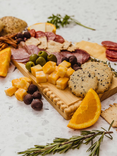 Serving board on counter covered in finger foods like cheeses, chocolates, and fruits.