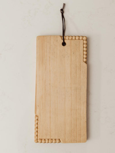 Small rectangular handmade serving board with circular detail carving on the top right and bottom left corners. Top of board contains a dark leather strap for hanging. 