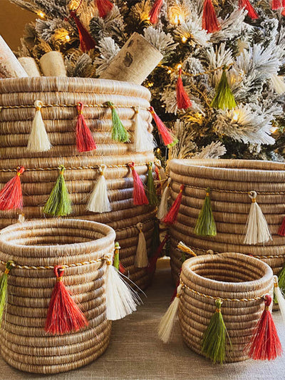 Red, green, and white tassel garland wrapped around woven baskets under a holiday tree. 