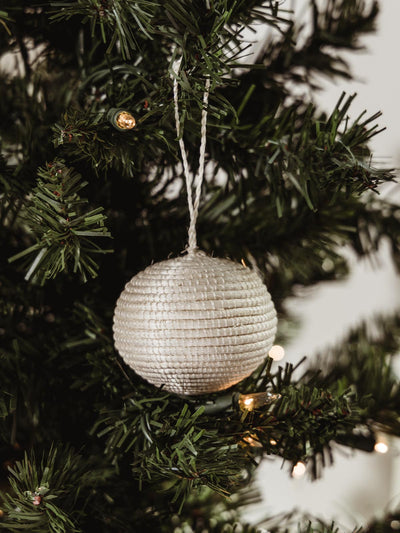 White woven ball ornament hanging on holiday tree.