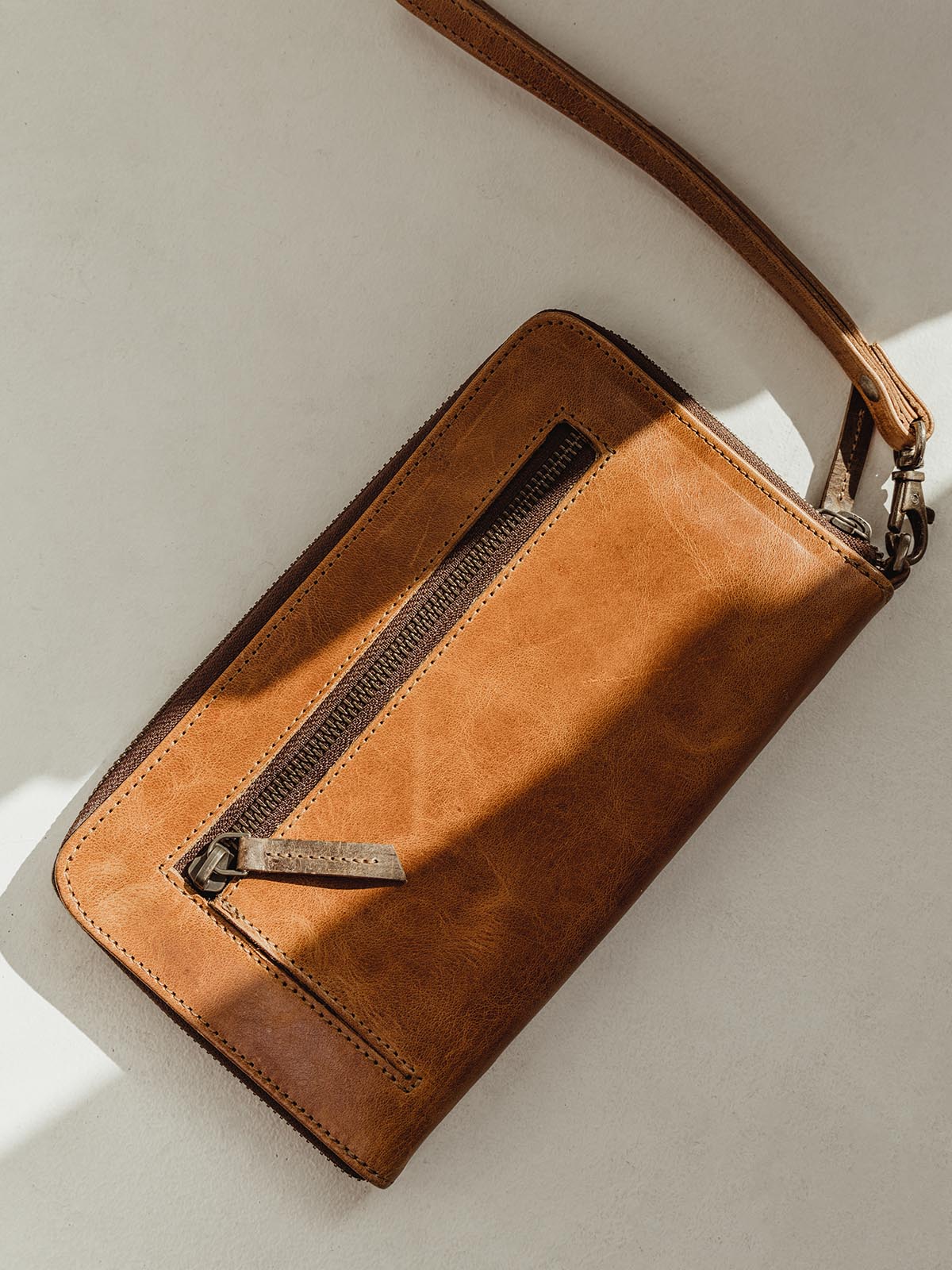 Backside of the closed Rani Wallet on a white table. Contains exterior zipper for additional storage. Leather wristlet can be added or removed. 