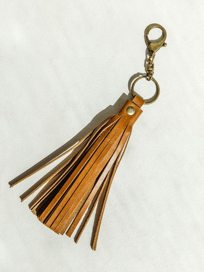 Leather fringe tassel with brass colored clip on a white background.