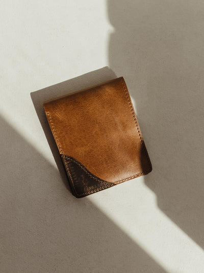 Closed compact hazelnut wallet with dark brown leather detail on corner of wallet. Wallet is placed on a cream table surface.