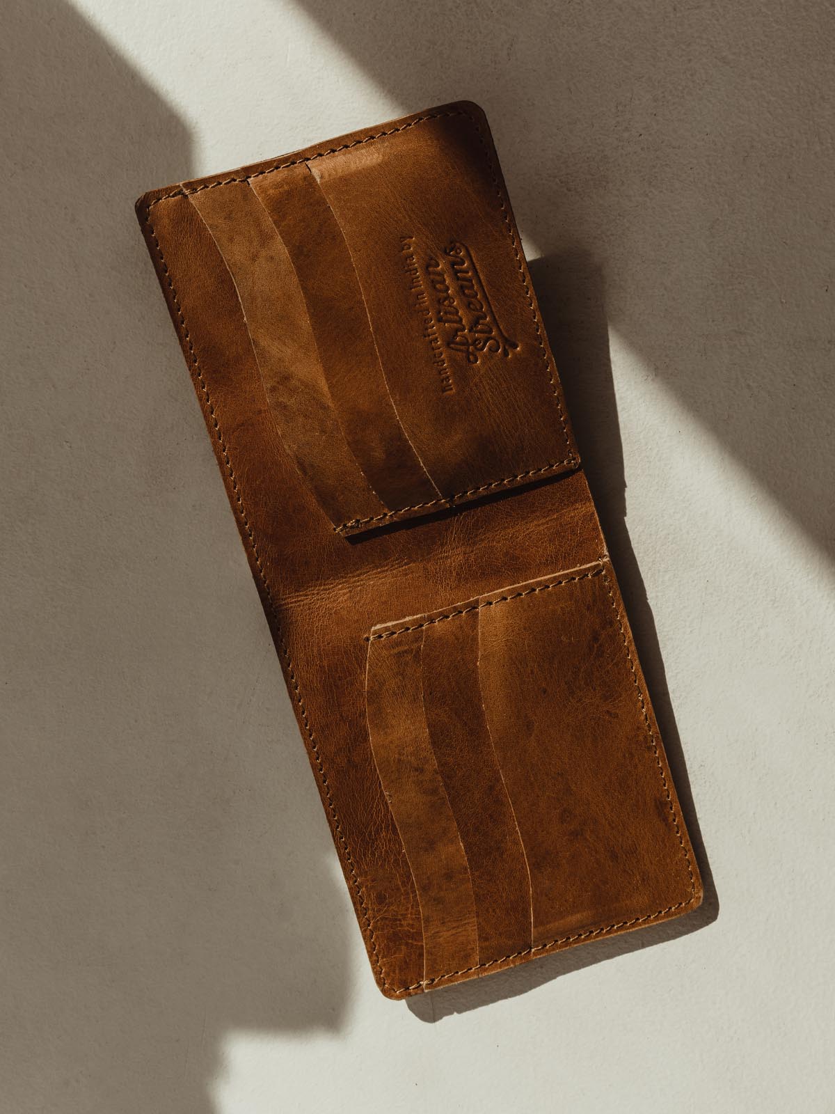 Open hazelnut colored wallet on cream background. Six small pockets for cards or IDs.