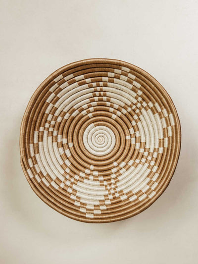 Large woven bowl on cream surface with white details in a diamond like pattern.