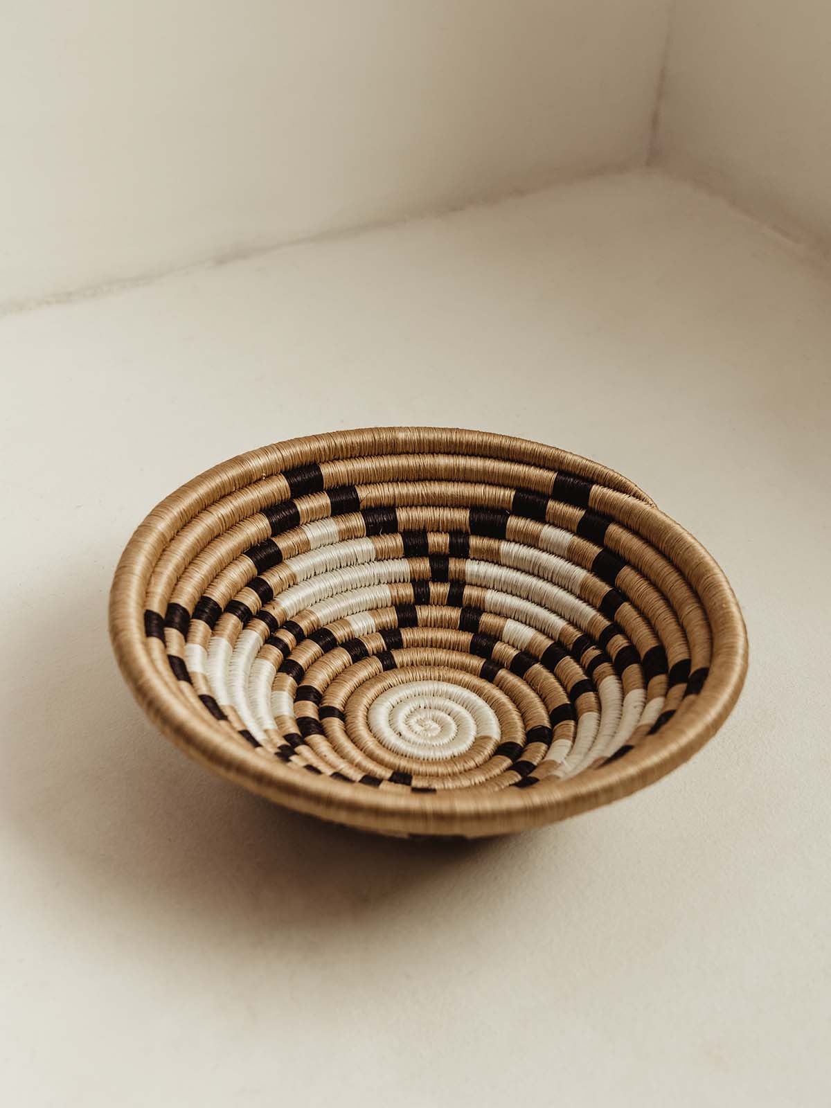Small Woven bowl on cream surface. Tan with black and white diamond patterns