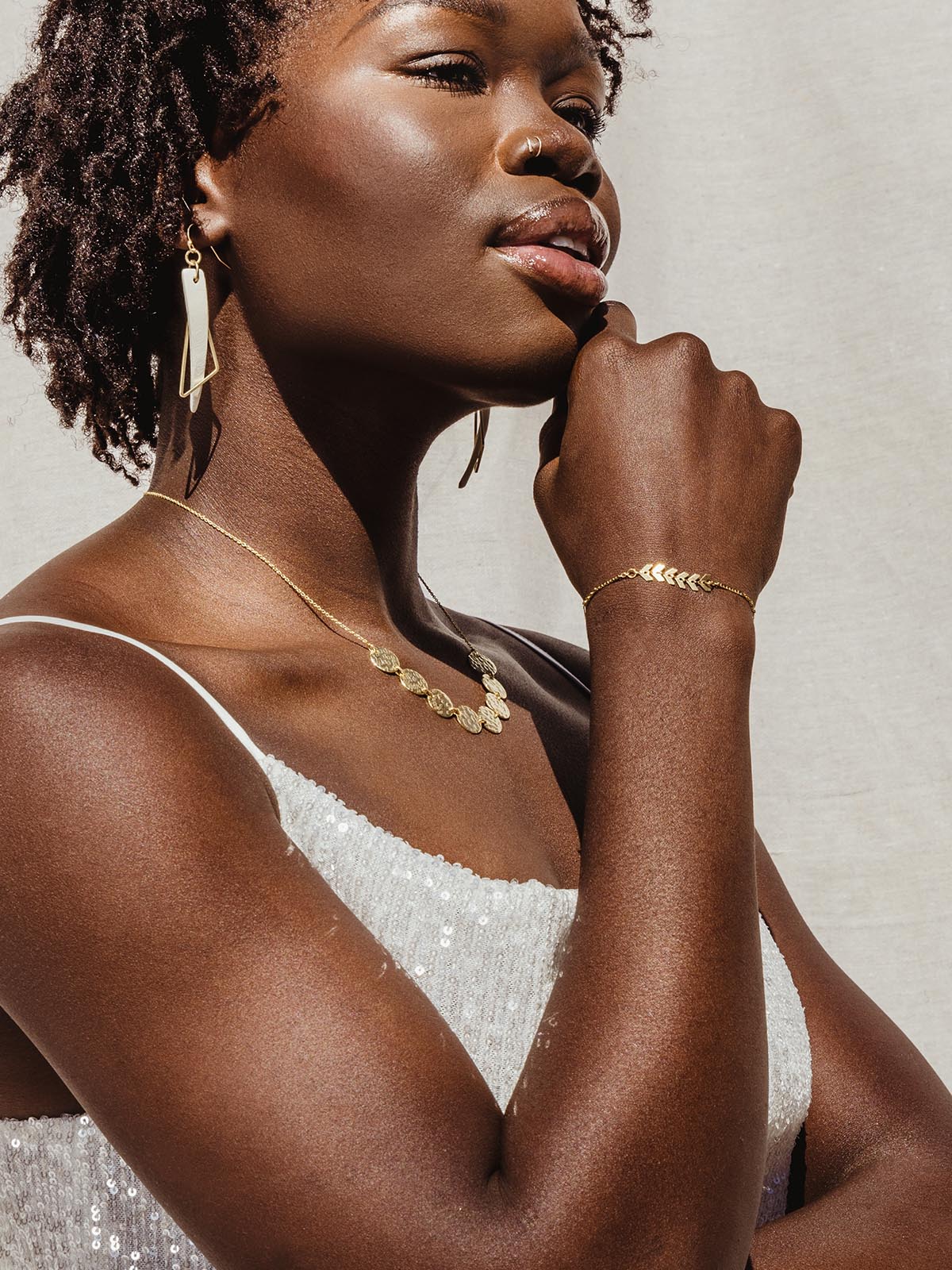 Female model wearing mini disc necklace with a white sparkle top and gold bracelet and earrings. 