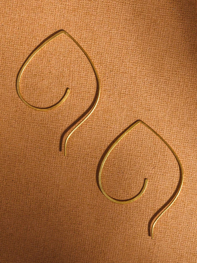 Pipal leaf brass earring on tan surface. 