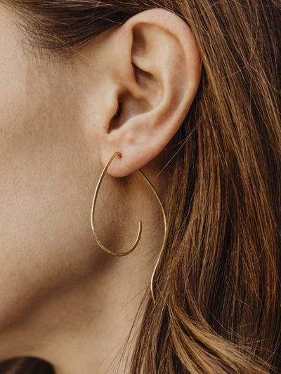 Close up of earring in models ear. Thin brass earring hangs from models ear.