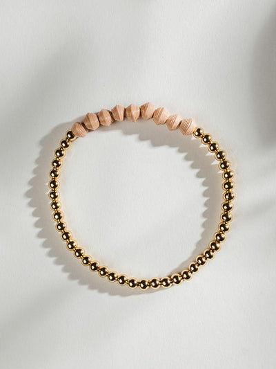 Golden beaded bracelet with nine peach beads on a white surface.