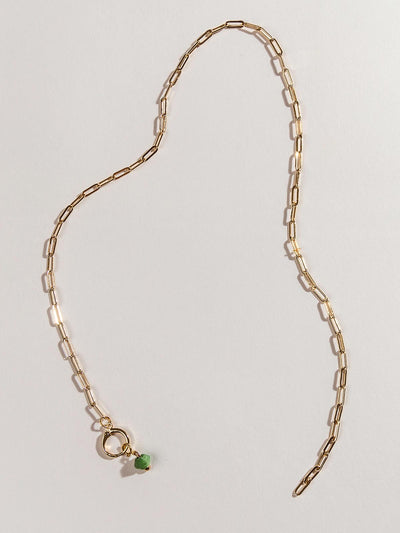 Golden chain charm necklace with one green birthstone bead on the clasp. Necklace is laid on a white surface.
