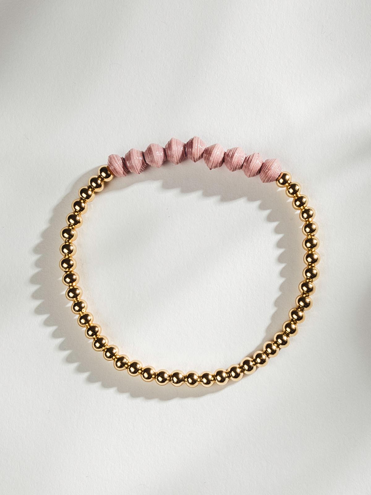 Golden beaded bracelet with nine pink beads on a white surface.