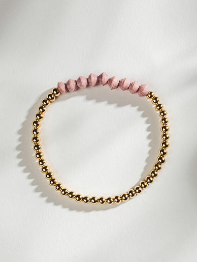 Golden beaded bracelet with nine pink beads on a white surface.