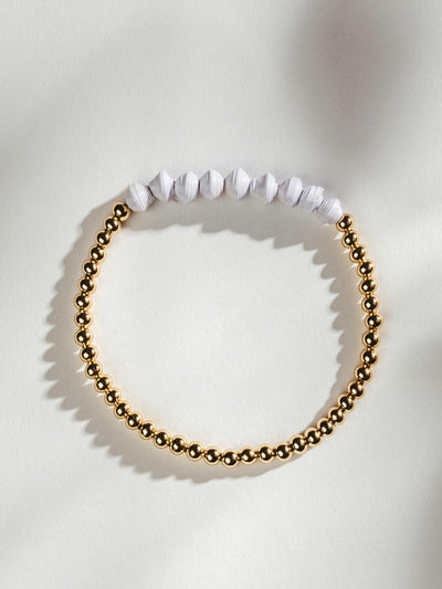 Golden beaded bracelet with nine white beads on a white surface.
