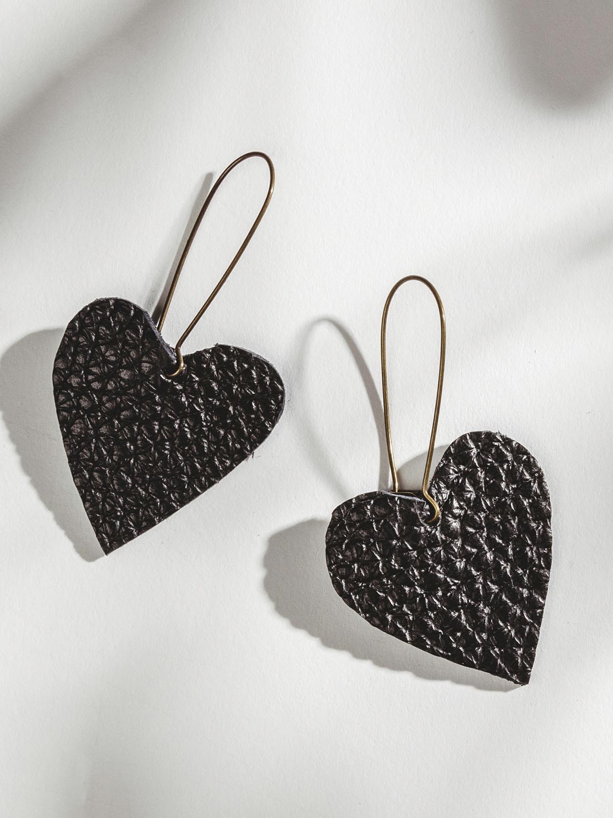 Black leather heart earrings on white surface.