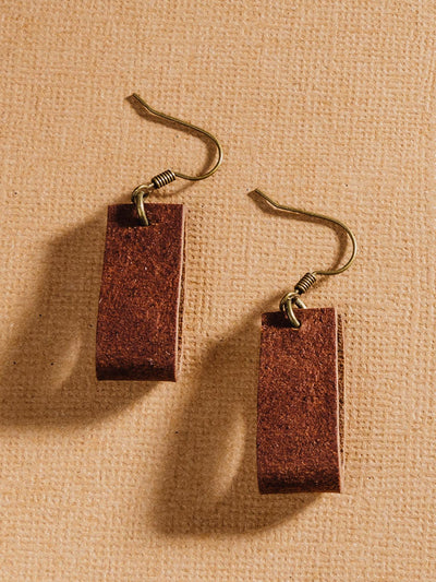 Small looped rectangular leather earrings on a tan surface.