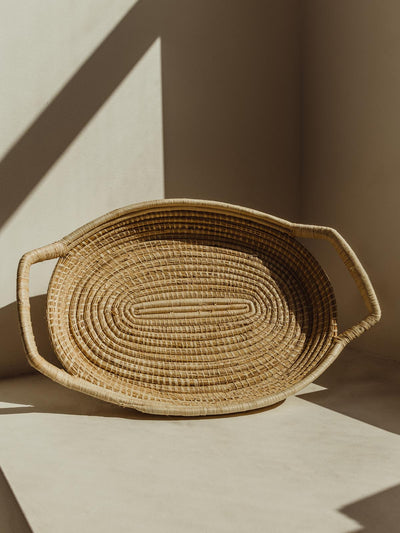 Large woven serving tray in a light tan color on a cream surface.
