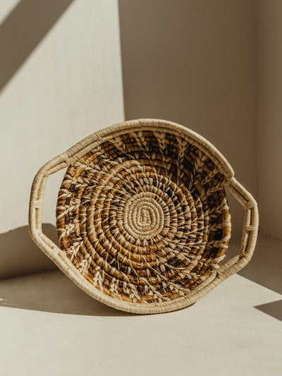 Small brown and tan woven basket with handles on cream surface.