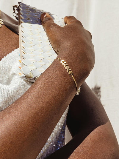 Female model wearing dainty golden bracelet with six arrow-like shapes.