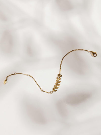 Dainty golden bracelet on white surface with six arrow-like shapes.