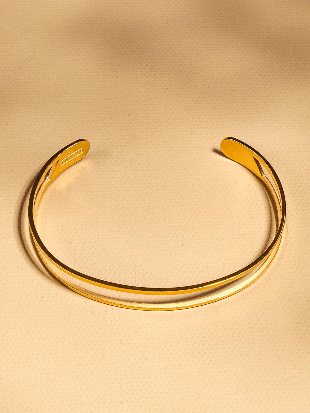 Golden cuff with split metal through the center of the braclet on tan background