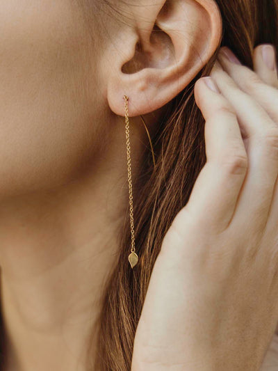 Female model wearing long earrings with small leaf shape on the end of the chain 
