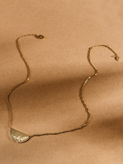 Half mood golden pendant with mustard seeds etched in the gold. Features quality golden chain on tan background.