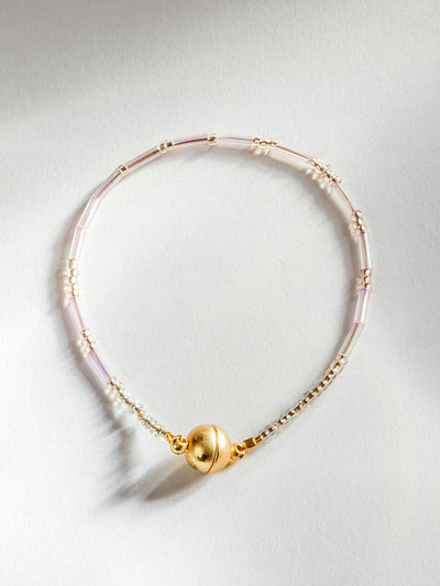 Thin bracelet with gold magnetic clasp. Beading is a clear blush pink color with gold bead accents.