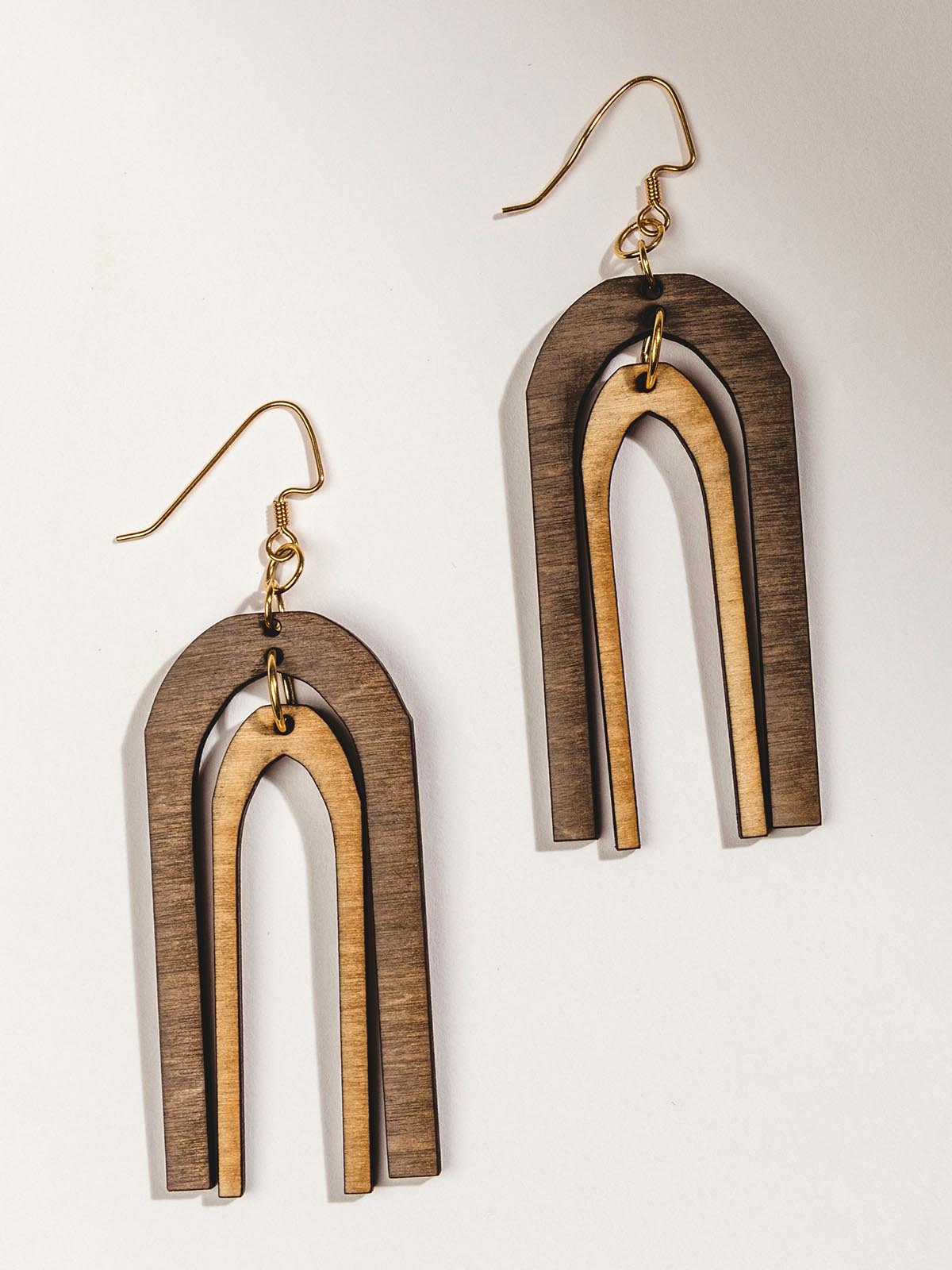 Wood earring on white surface with dark brown arch shape layer over a light brown arch shape. Shapes are separate and move freely. 
