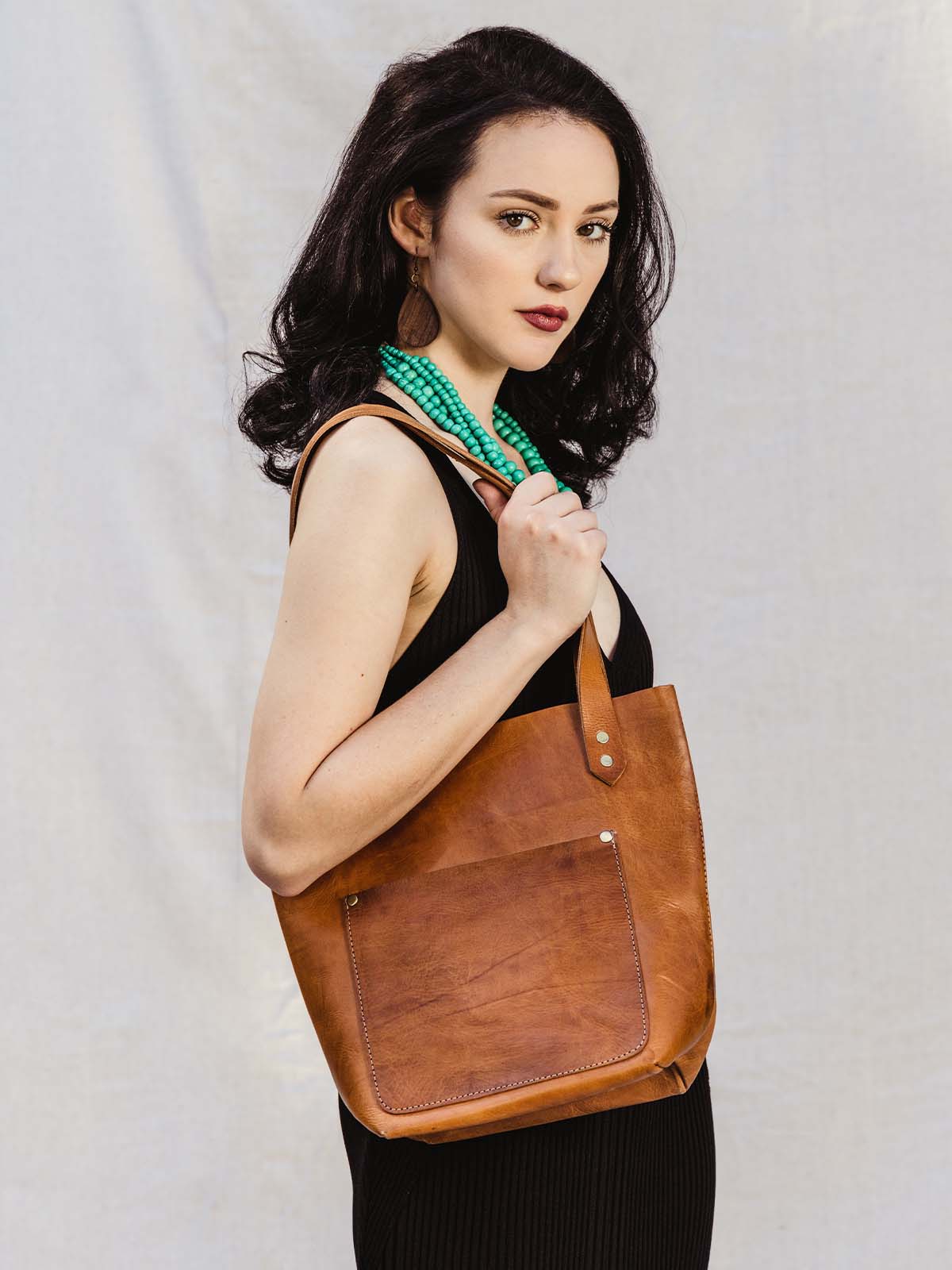 Female model holding hazelnut colored leather handbag over the shoulder.