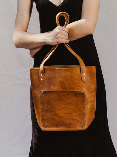 Close up of female model holding hazelnut colored leather hand bag with large front pocket.
