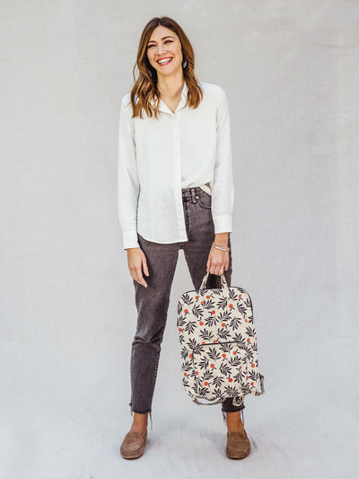 Female model holding berry patterned backpack by top handle on a white background.