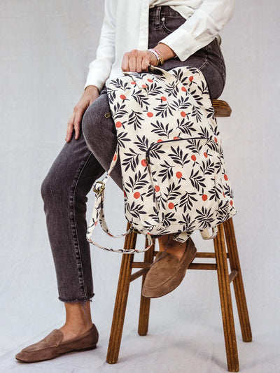 Female model sitter on a stool holding Very patterned backpack.
