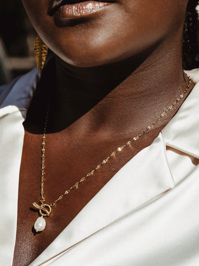 Female model wearing long golden chain necklace with pearl pendant 