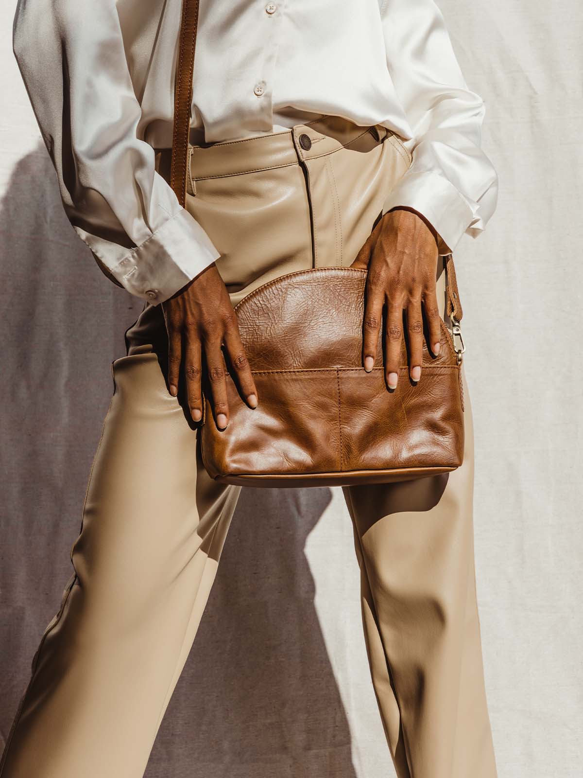 Female model holding half moon leather hand bag across the body. Leather bag has two front pockets.