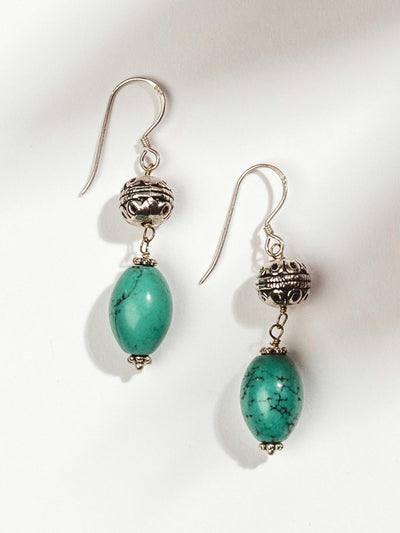 Silver bead earrings with turquoise dangle on white surface.