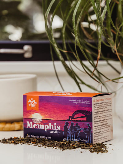 Memphis Medley Tea box on counter with coffee cup and greenery.