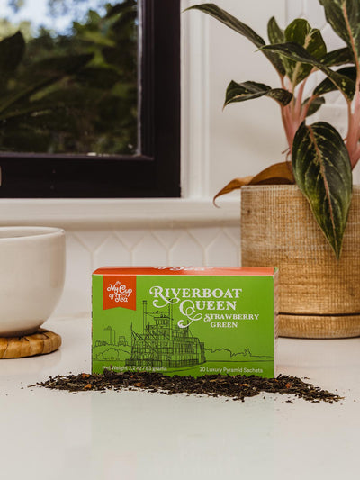 Strawberry Green Tea box on counter with coffee cup and greenery.