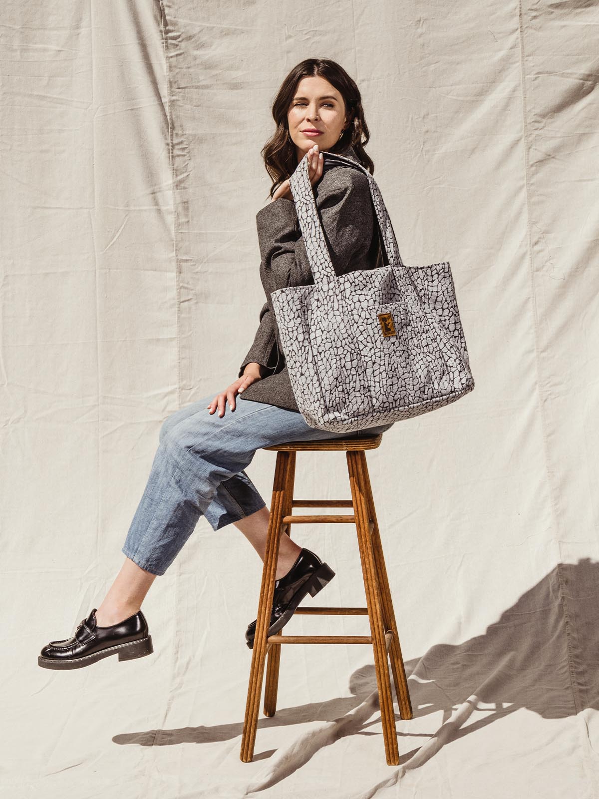 Female model sitting on stool holding large grey textured tote bag