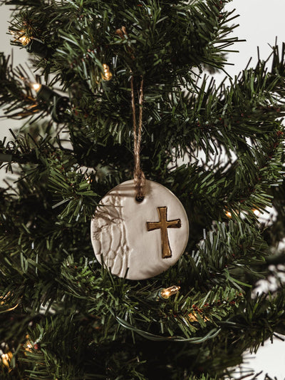 Ceramic circle with texture and golden cross hangin on holiday tree.
