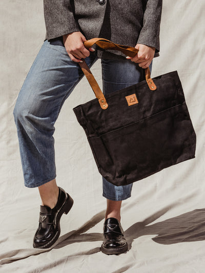 Model holding black tote bag with leather straps on a cream backdrop