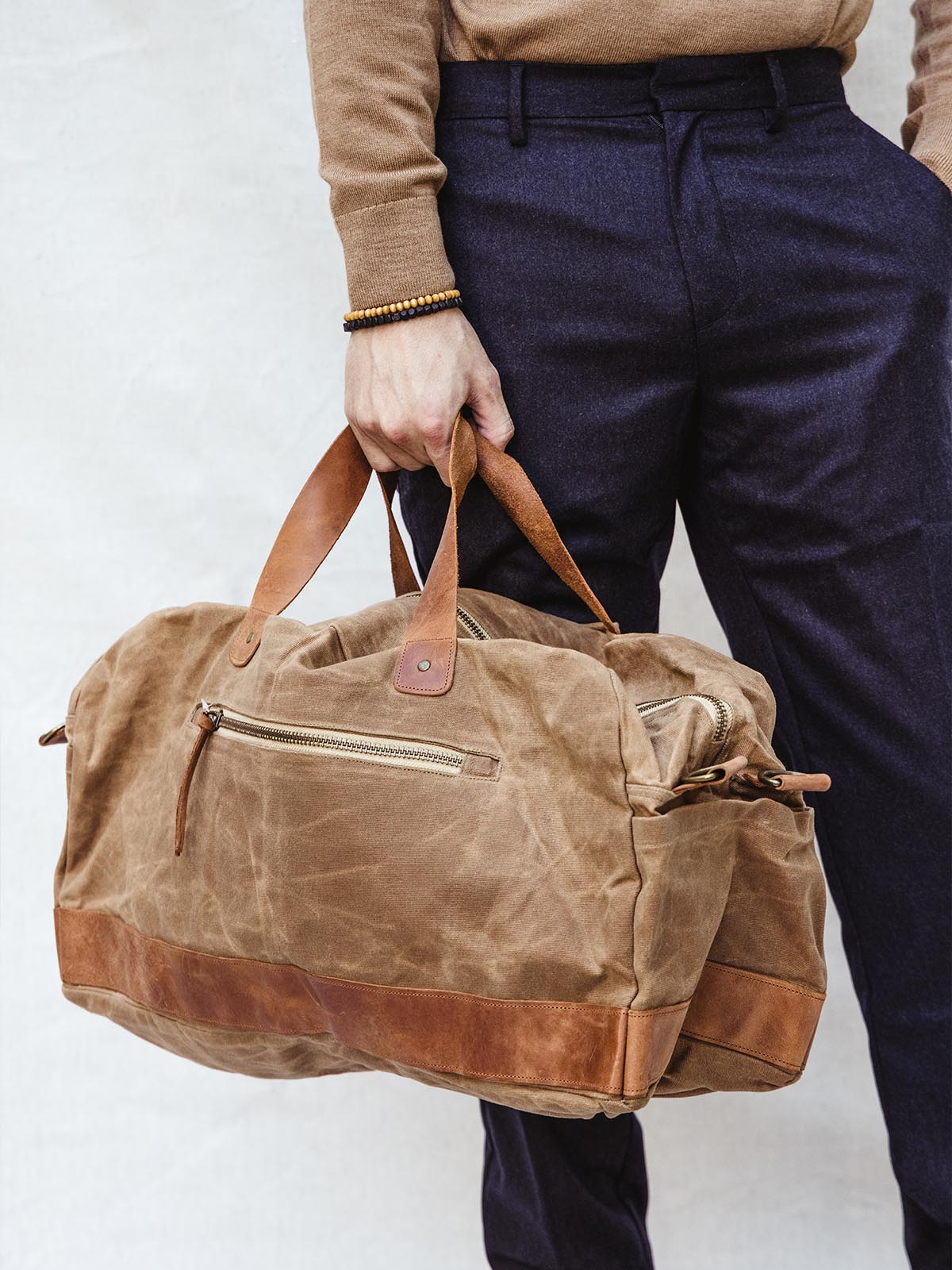 Male model carrying tan weekender bag in hangs without crossbody strap/